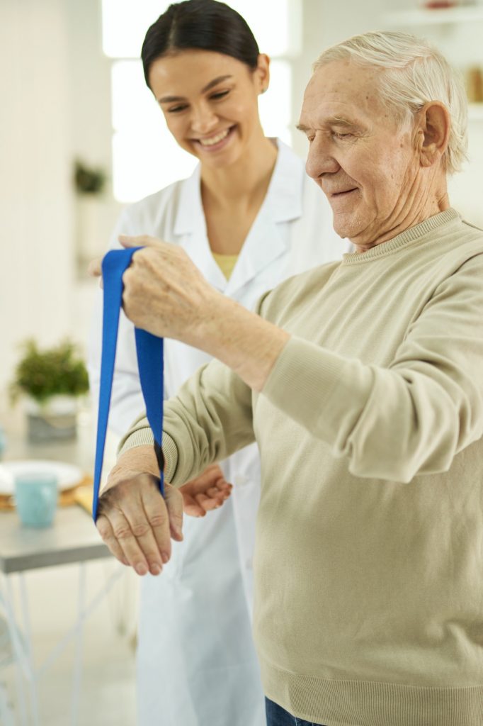 Smiling elderly man and young nurse looking at fitness rubber